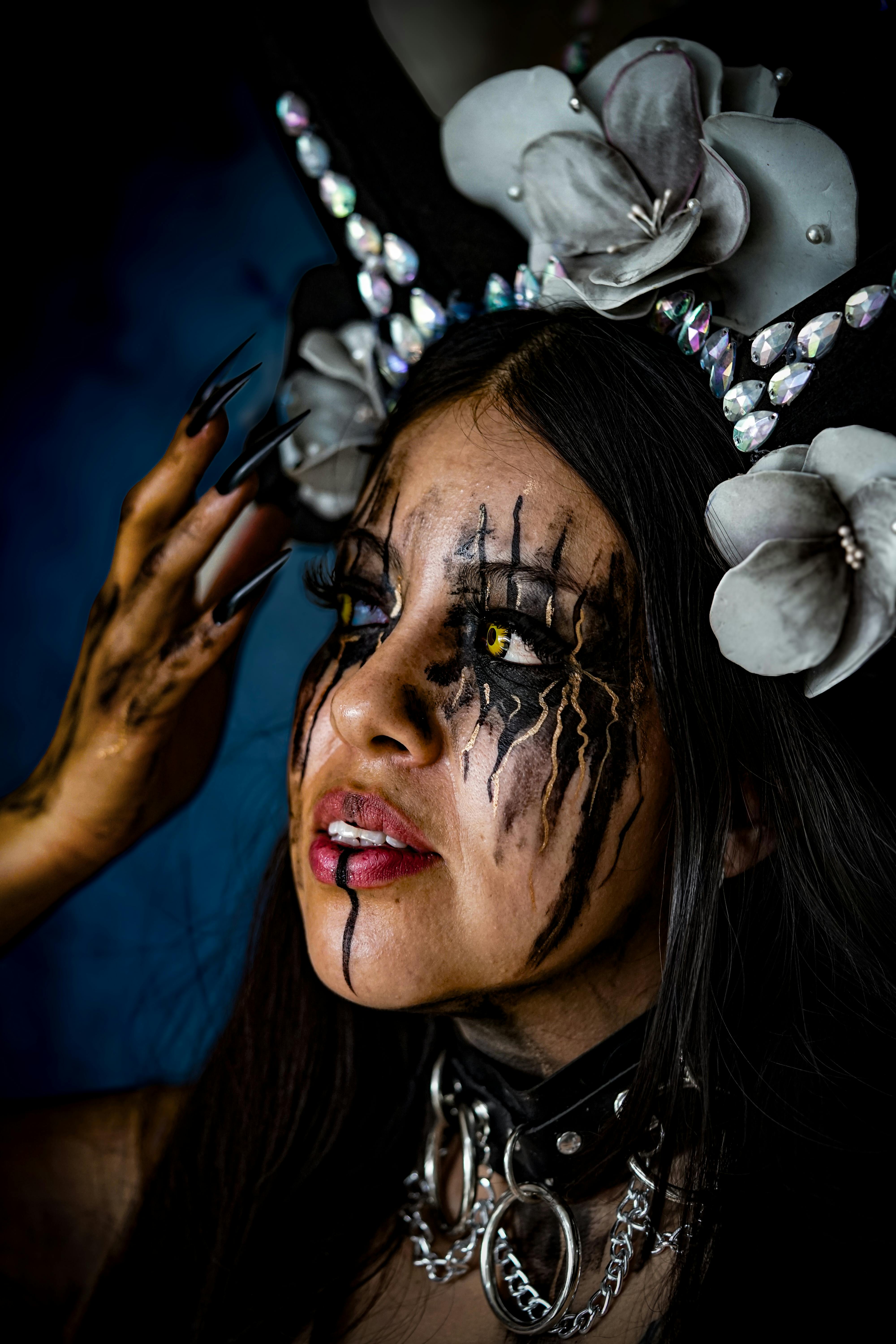 Close-up of a woman in fantasy makeup with dramatic eyeliner and floral headpiece.