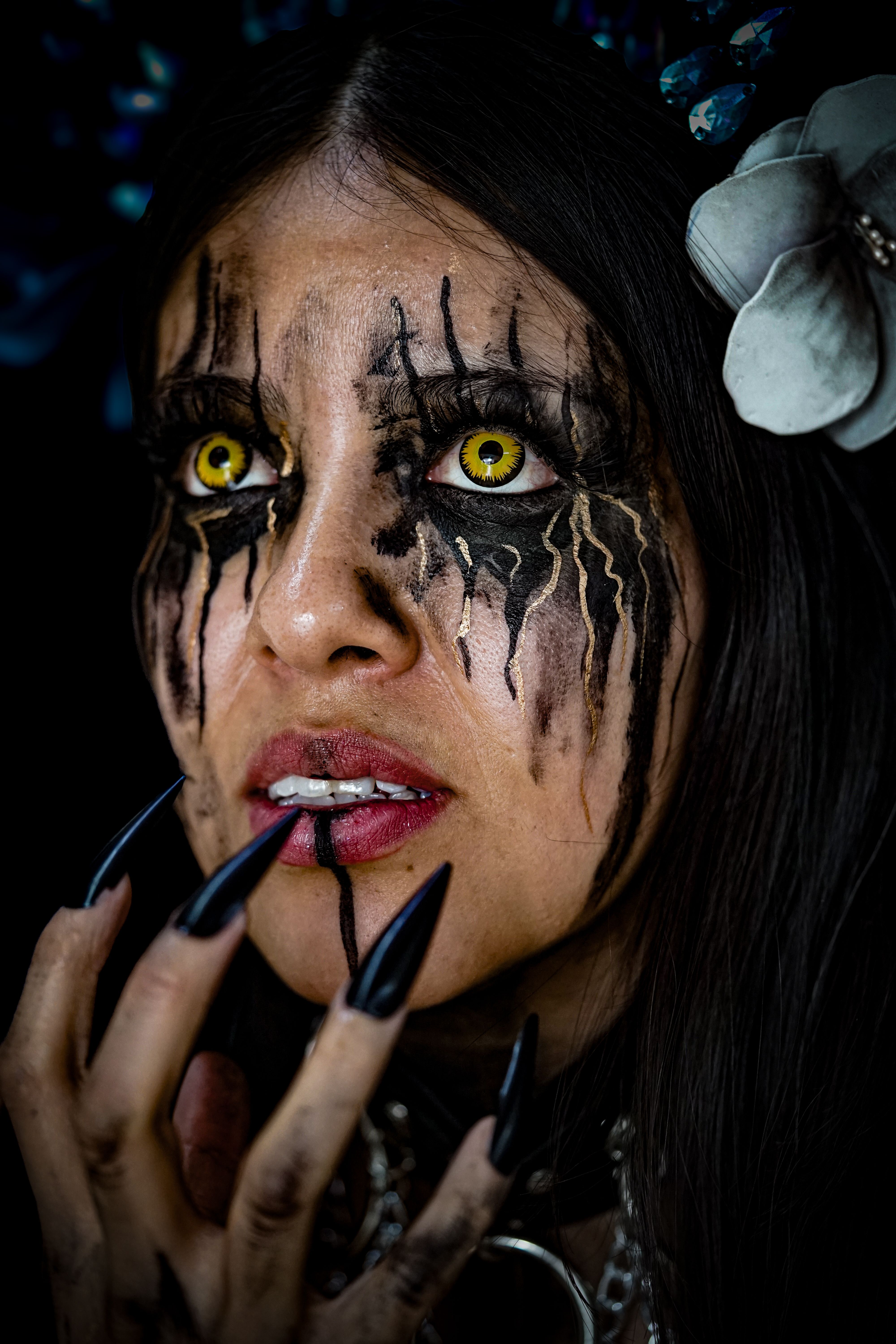 Close-up of a woman with gothic makeup, yellow eyes, and black nails, exuding a mysterious aura.
