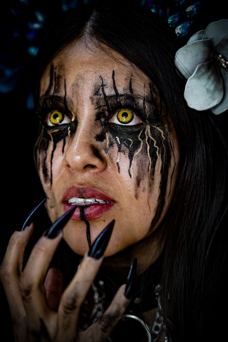 Close-up of a woman with gothic makeup, yellow eyes, and black nails, exuding a mysterious aura.