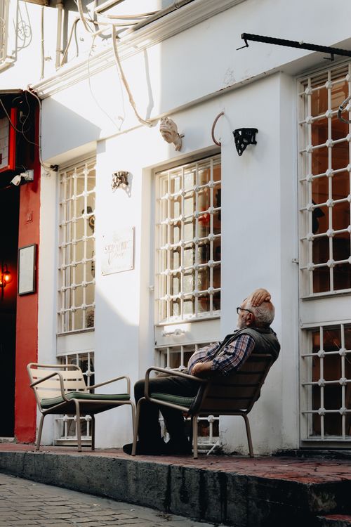 Free Senior man sitting outside a café, enjoying a peaceful afternoon in an urban setting. Stock Photo