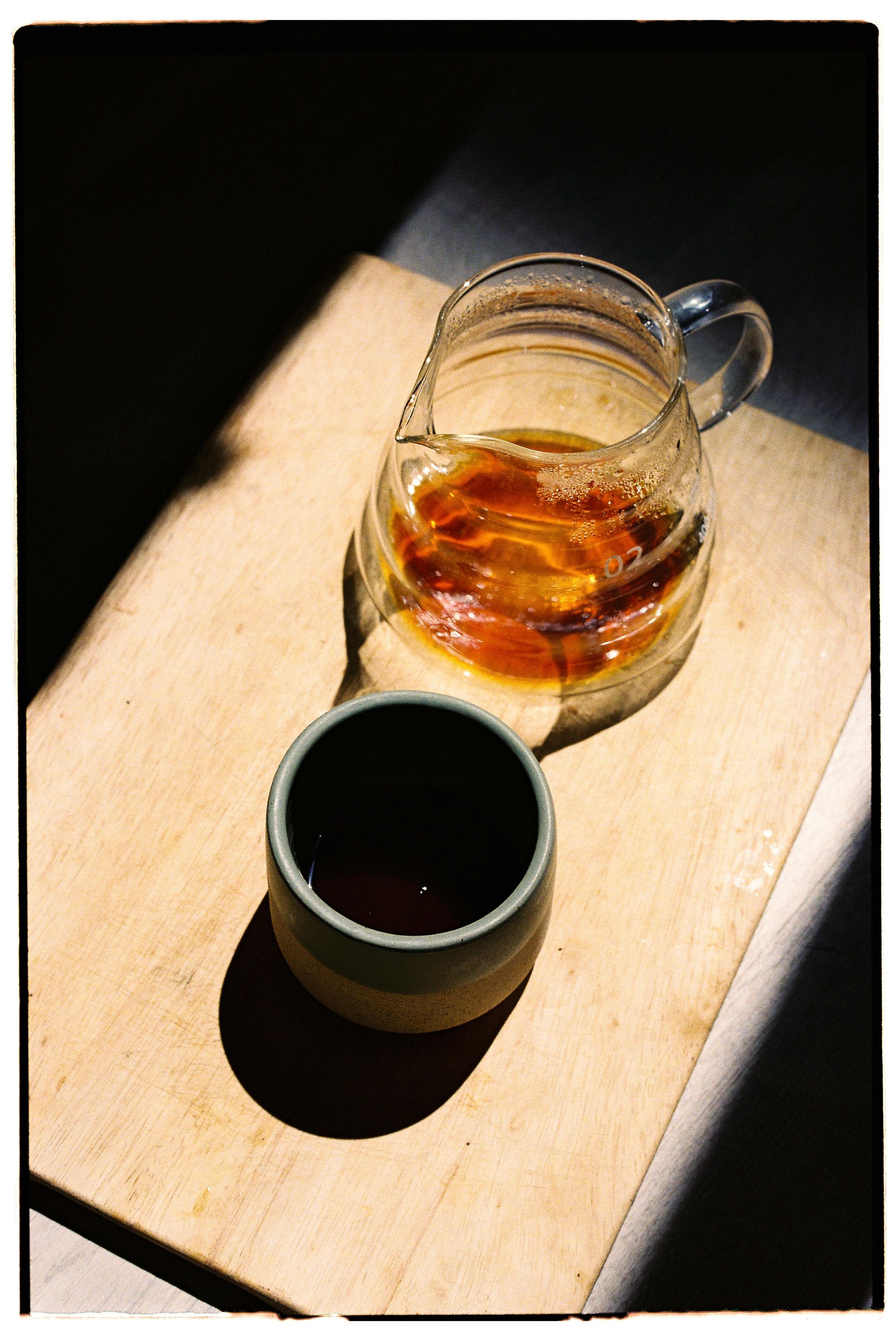 A warm, minimalist tea scene with a glass teapot and ceramic cup on wood.