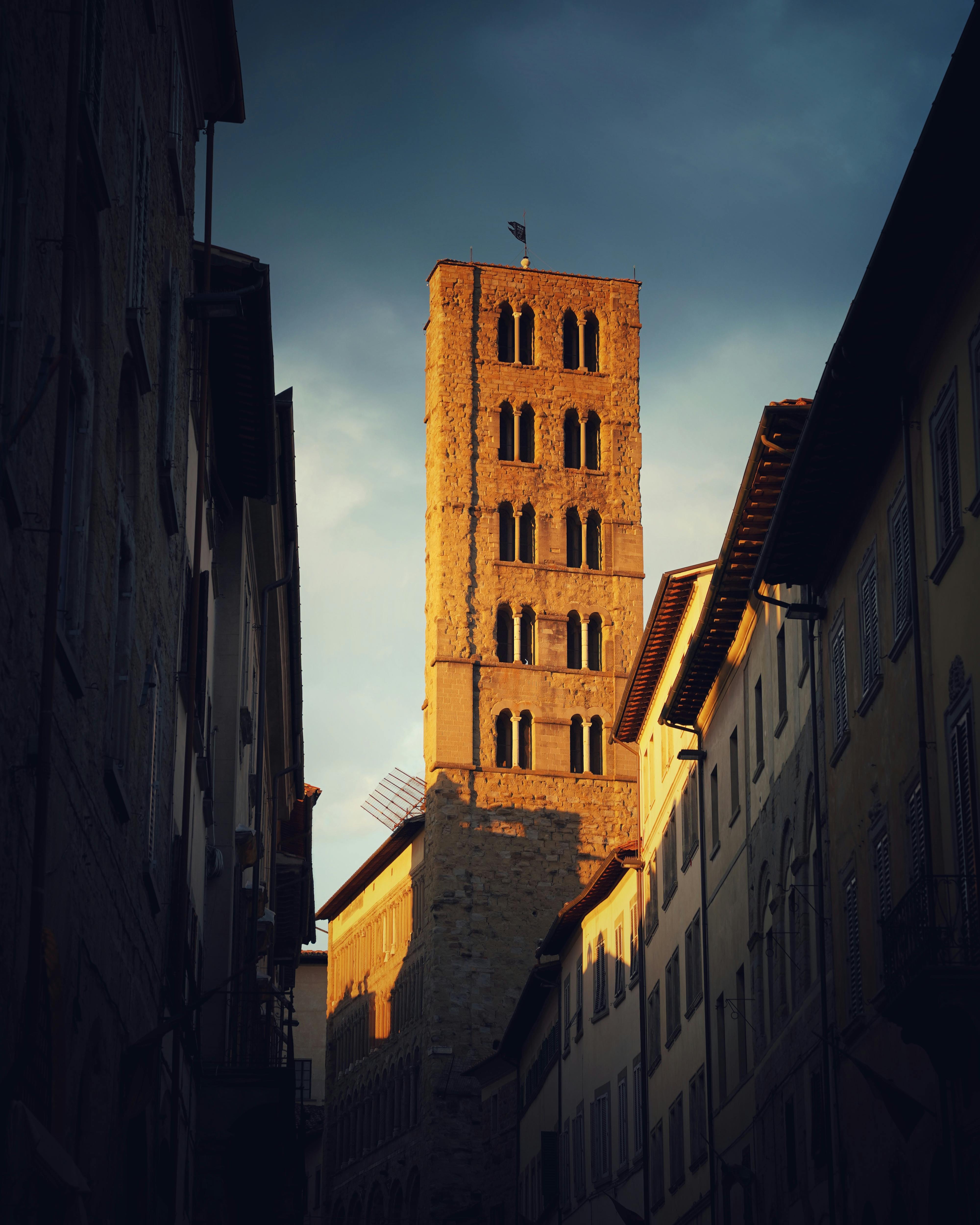 A striking historic tower in an Italian city, bathed in warm sunset light, with dramatic shadows.