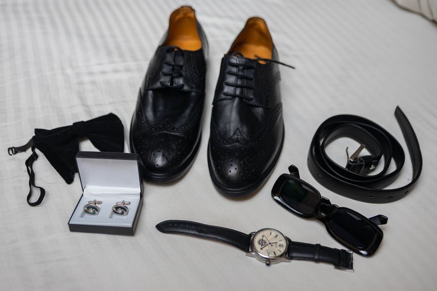 Men's accessories flat lay on white with dress shoes, sunglasses and cufflinks