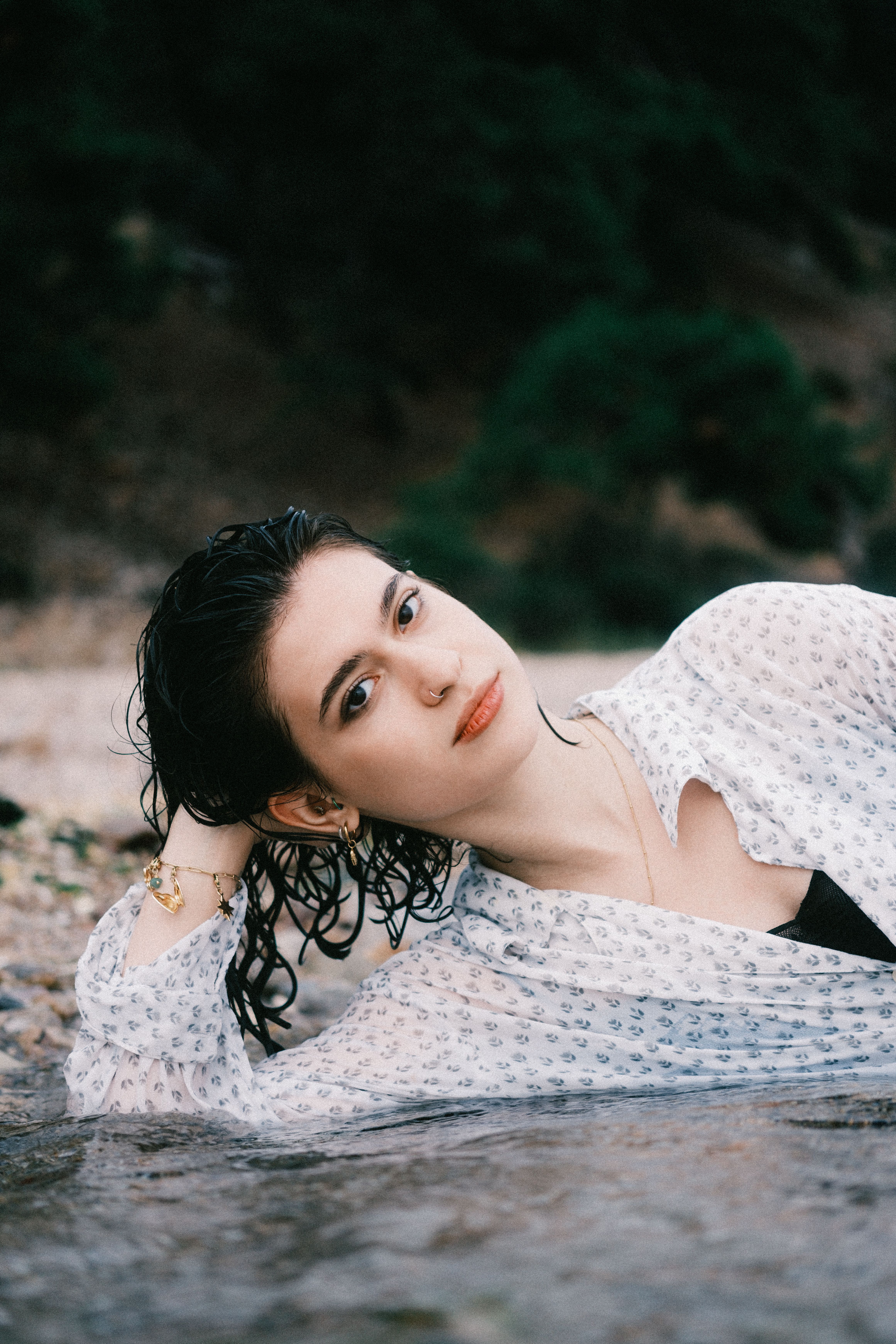Young woman with wet hair reclining by a riverbank, exuding a serene and summery vibe.