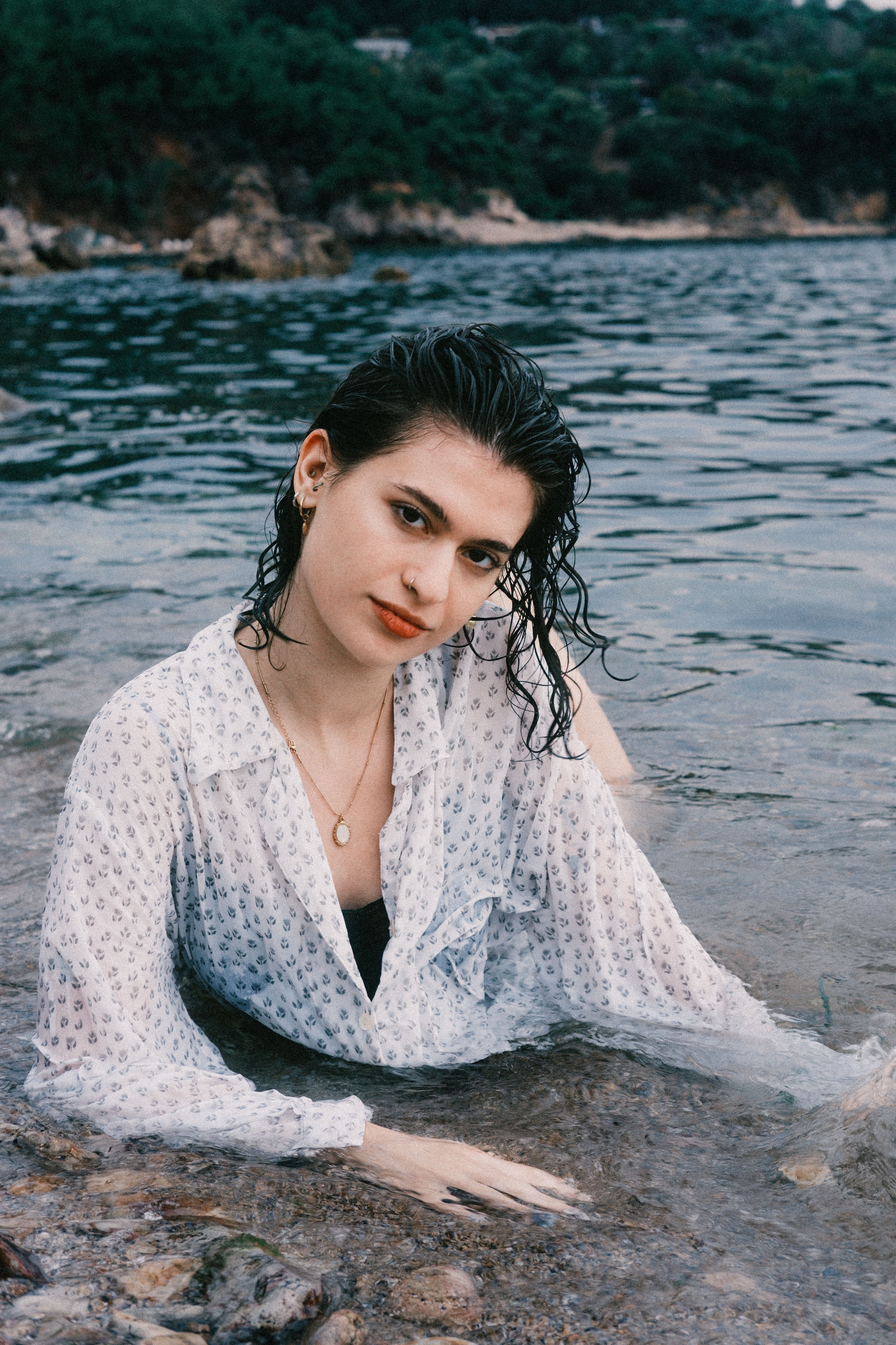 A young woman in a white blouse relaxes in the water by a rocky shoreline, exuding tranquility.