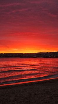 Stunning red and orange sunset over a tranquil beach and ocean waves.