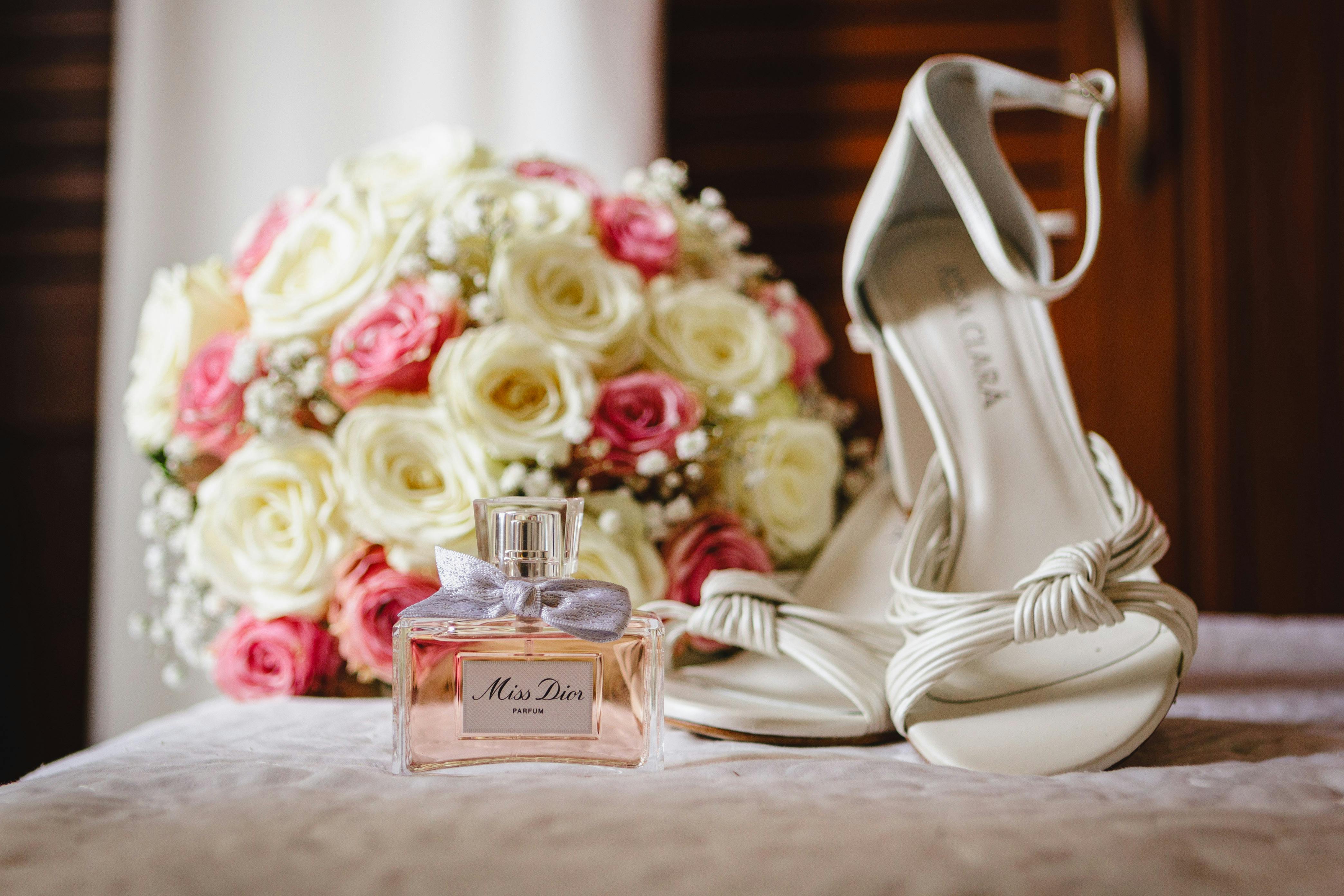 Free Romantic bridal setup featuring a Dior perfume, bridal shoes, and a bouquet of roses. Stock Photo
