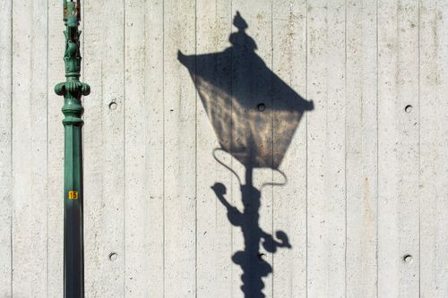 Free Street lamp casting a detailed shadow on a textured concrete wall in bright daylight. Stock Photo