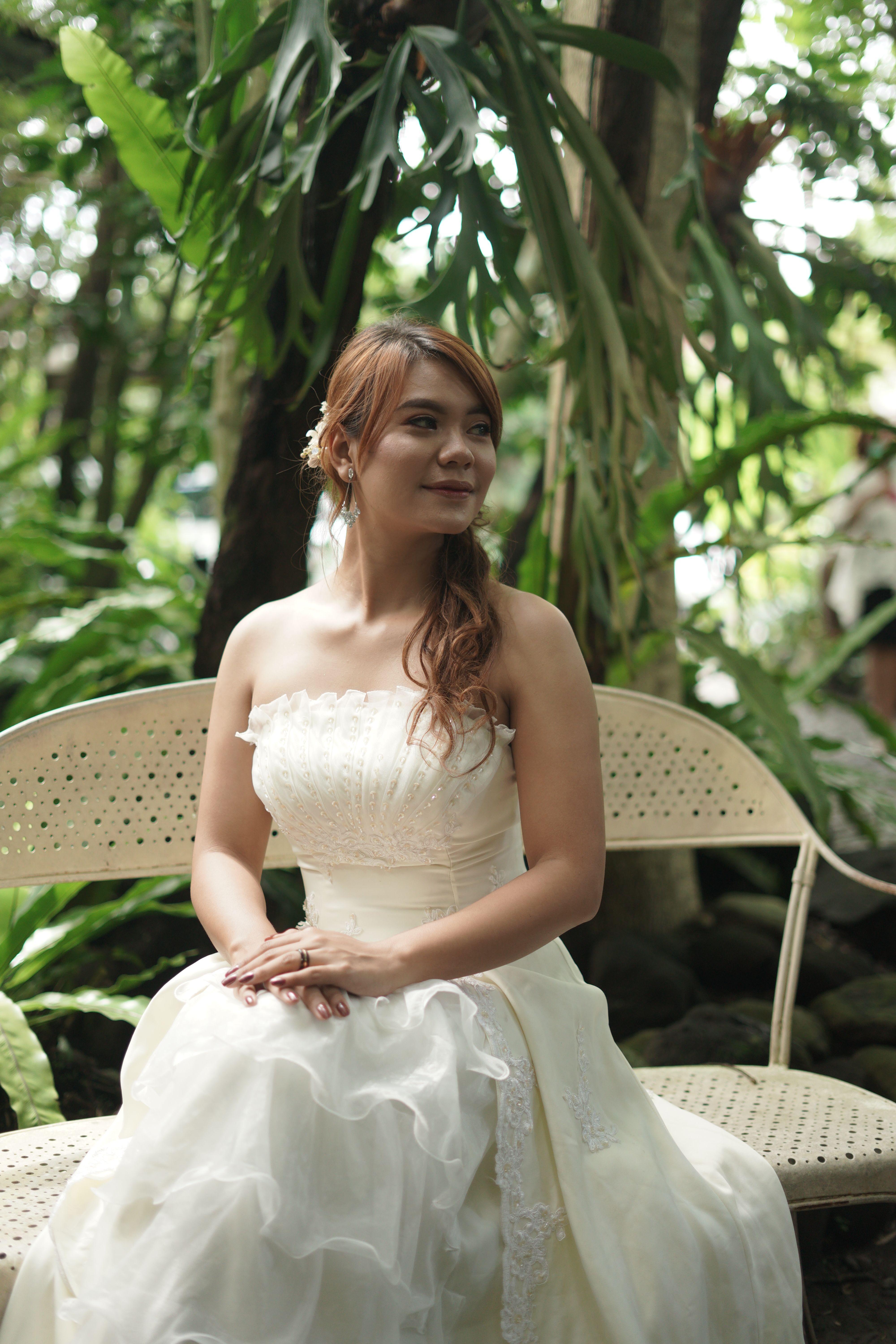 A beautiful asian bride in a classic wedding dress seated in a verdant garden setting, capturing elegance and romance.