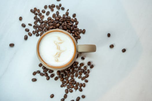 Top view of a cappuccino surrounded by coffee beans on a marble background.