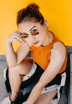 一位时尚女性戴着墨镜，在亮黄色的墙壁旁摆姿势