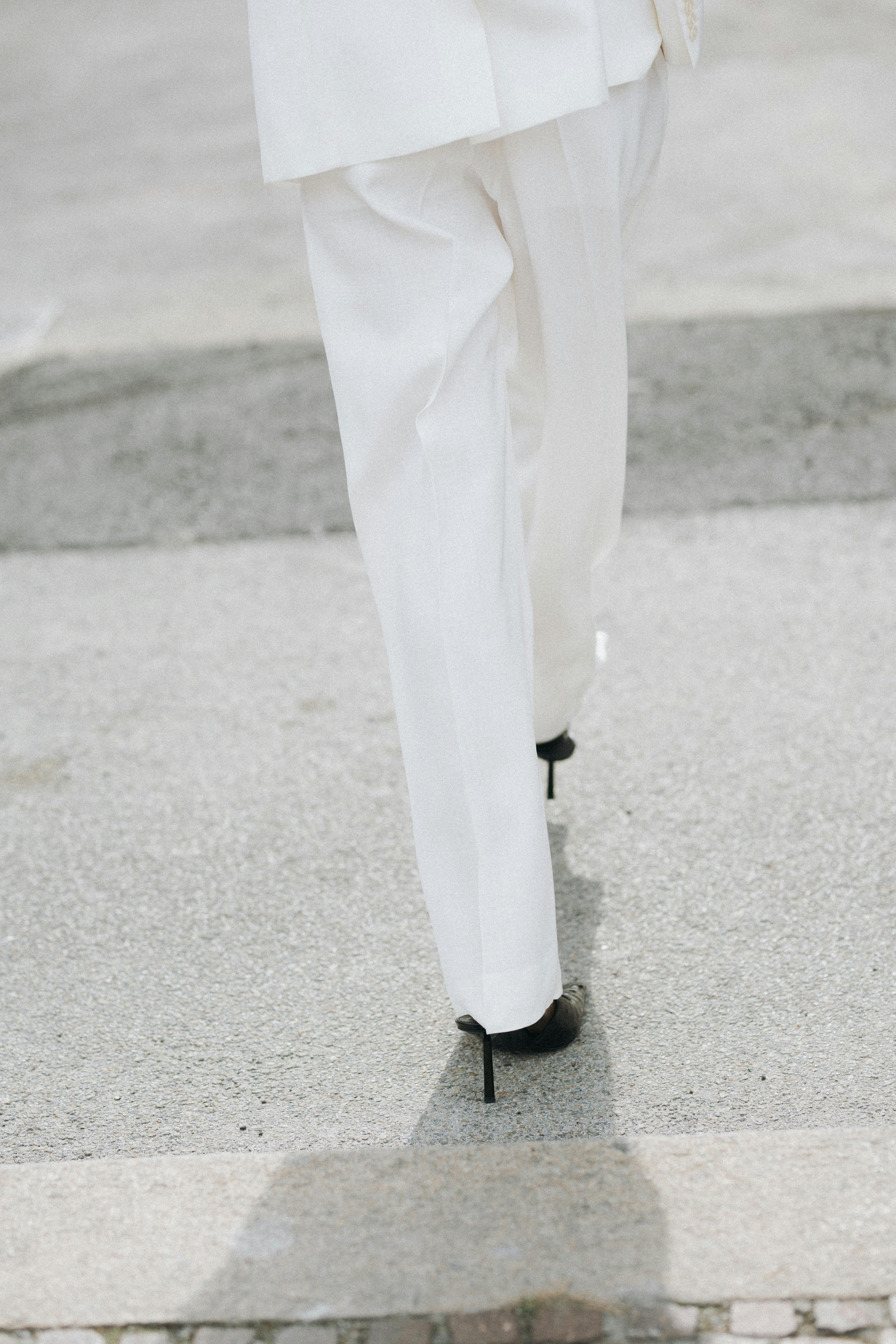 Stylish woman in a white suit and black heels walking outdoors.