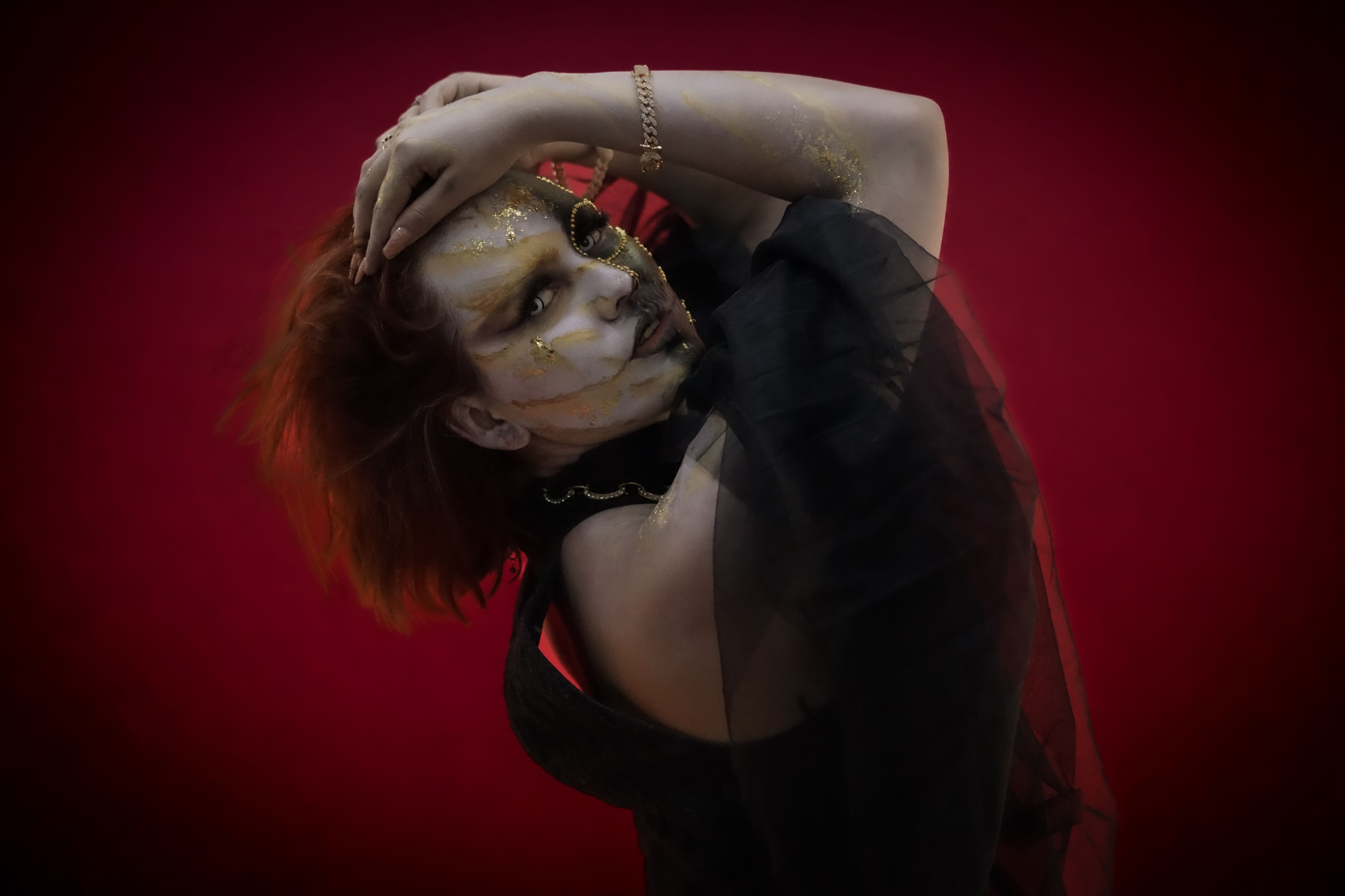 A creative portrait featuring gold makeup and dramatic expression on a red backdrop.