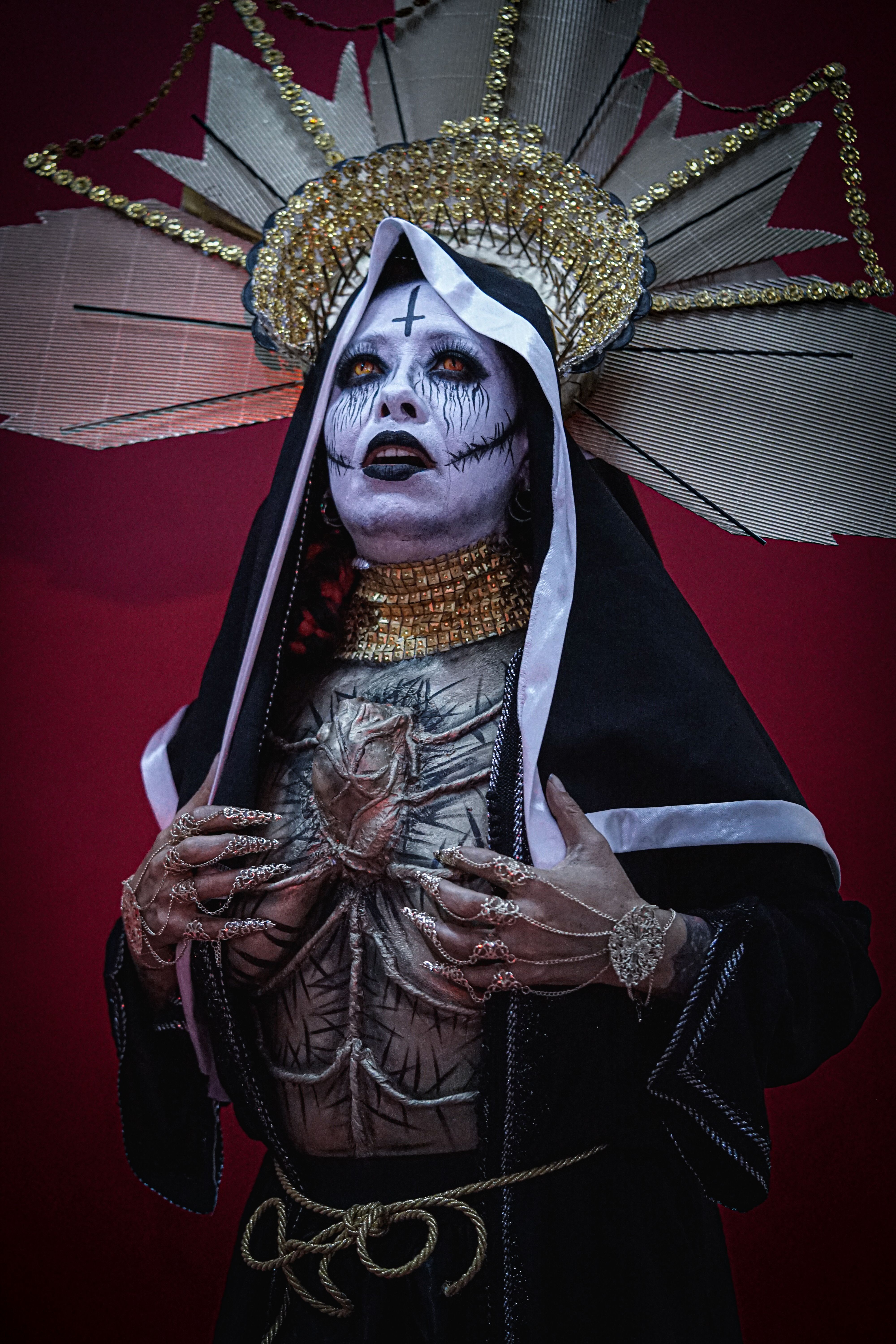 Person in elaborate gothic costume with religious imagery, theatrical makeup.