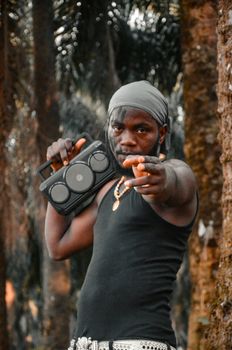 A strong expression of confidence as a man points while holding a boombox amidst trees.