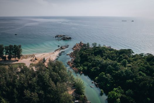Explore the serene landscape of Tanjung Balau's coastline captured from above, showcasing lush greenery and calming waters.