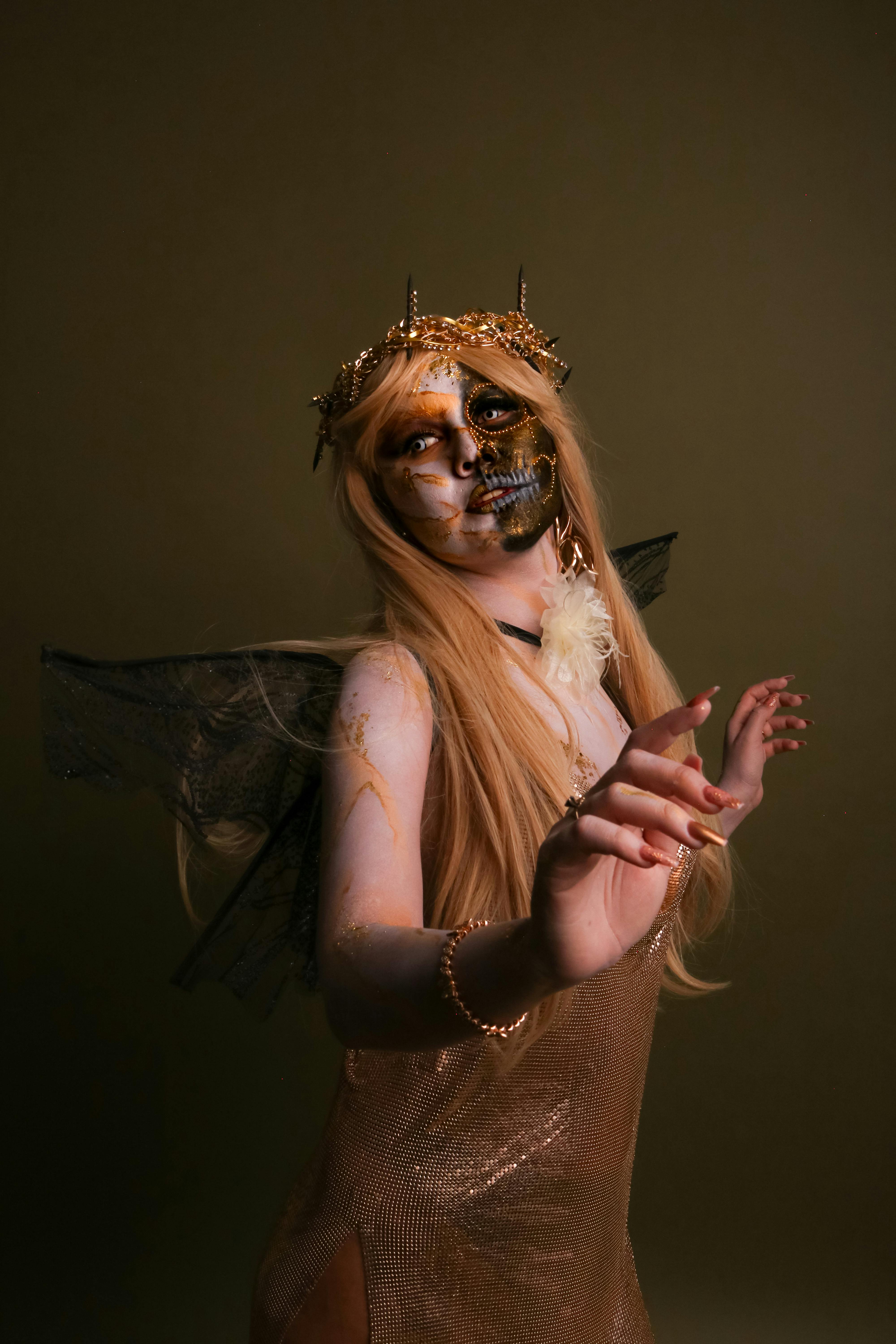 Woman dressed in fantasy outfit with artistic makeup and wings, dramatic lighting.