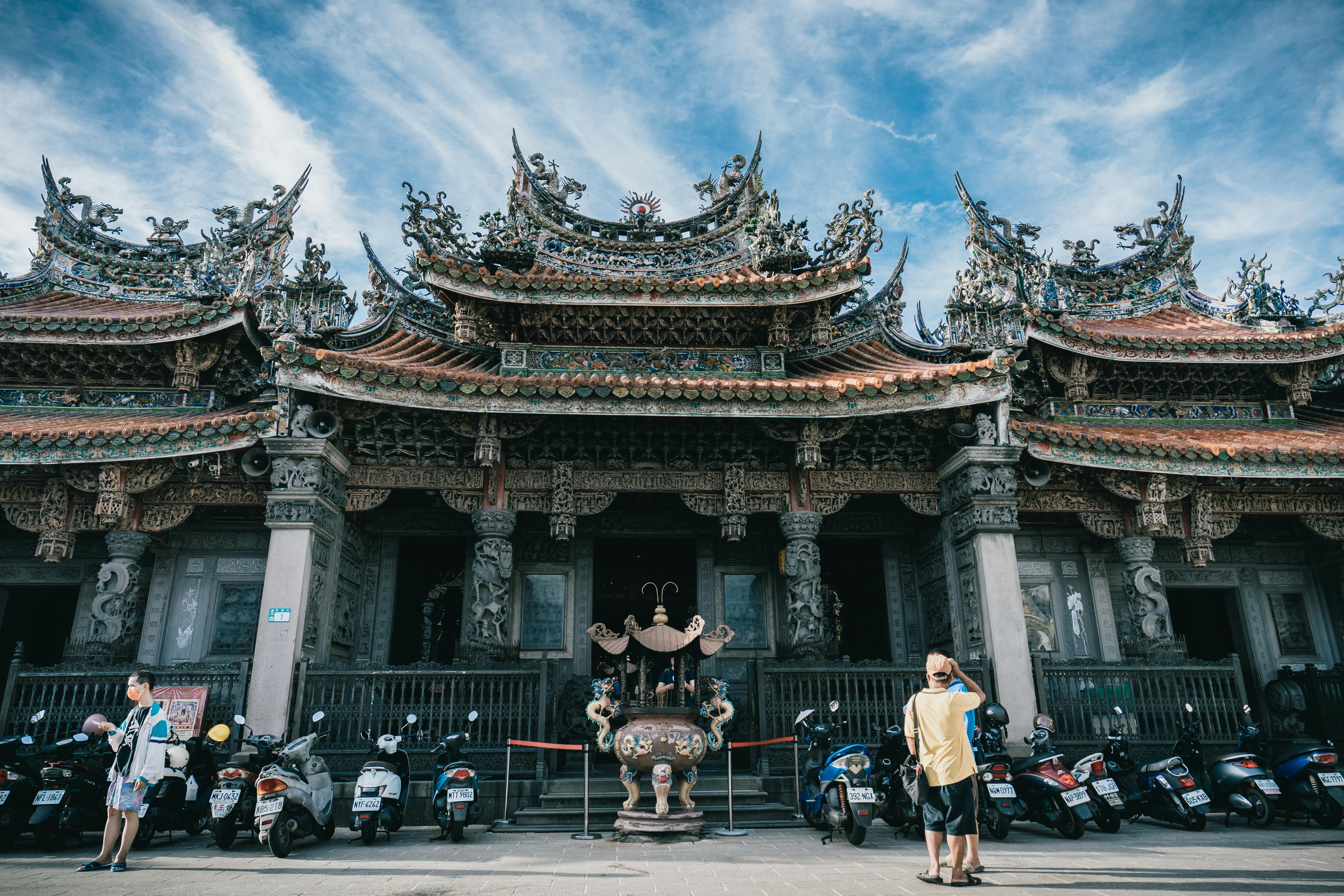 Captivating view of an intricate temple facade with visitors and parked scooters.