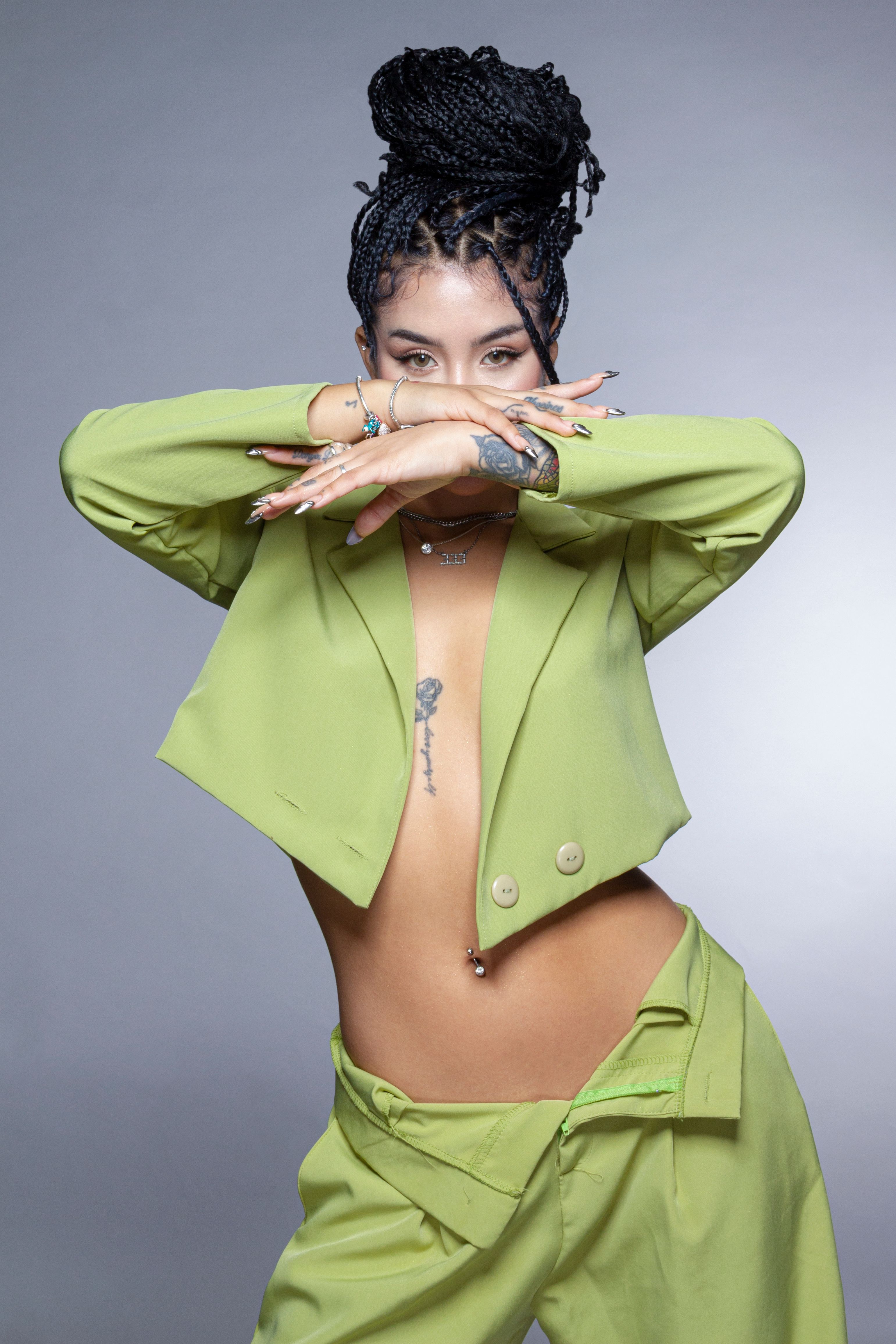 Portrait of a fashionable woman in a vibrant green suit, showcasing unique tattoos and braided hairstyle.