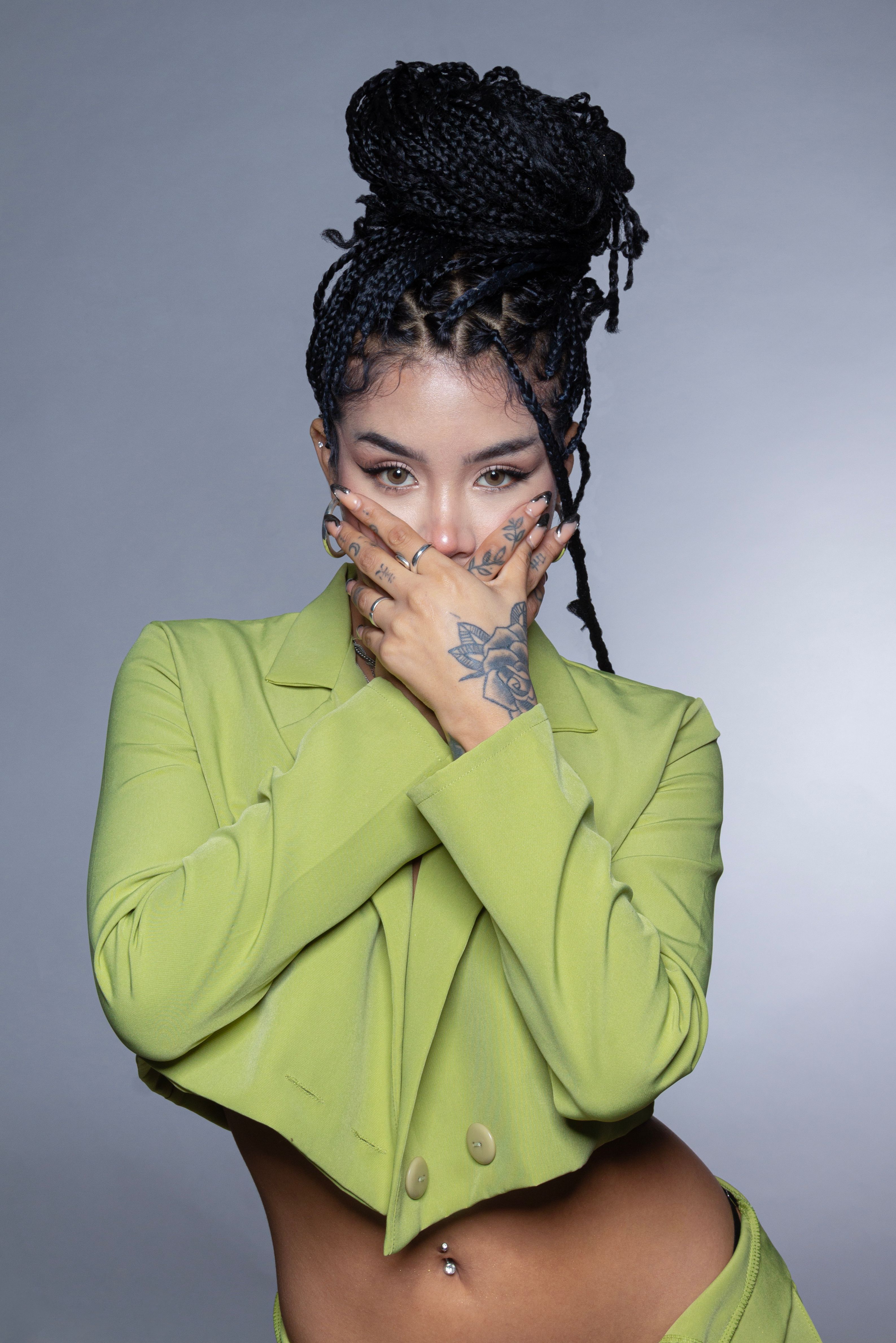 A woman with braided hair and tattoos striking a pose in a lime green outfit.