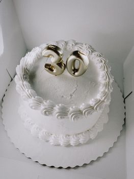 A white vanilla cake with gold '30' candles for a 30th birthday celebration.