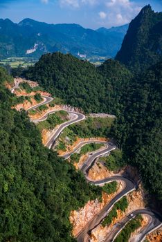 Aerial view of a winding mountain road through lush green landscape under a clear blue sky.