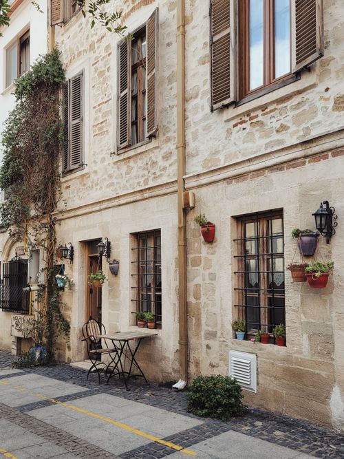 Free Cozy street view of a rustic stone house with hanging flowerpots and vintage shutters. Stock Photo