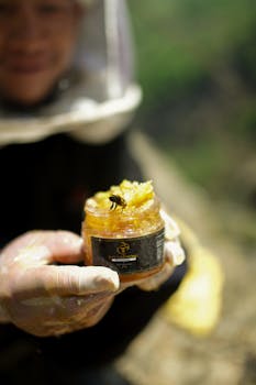 Close-up of a beekeeper in Nepal holding a jar of organic honey with a bee on it.