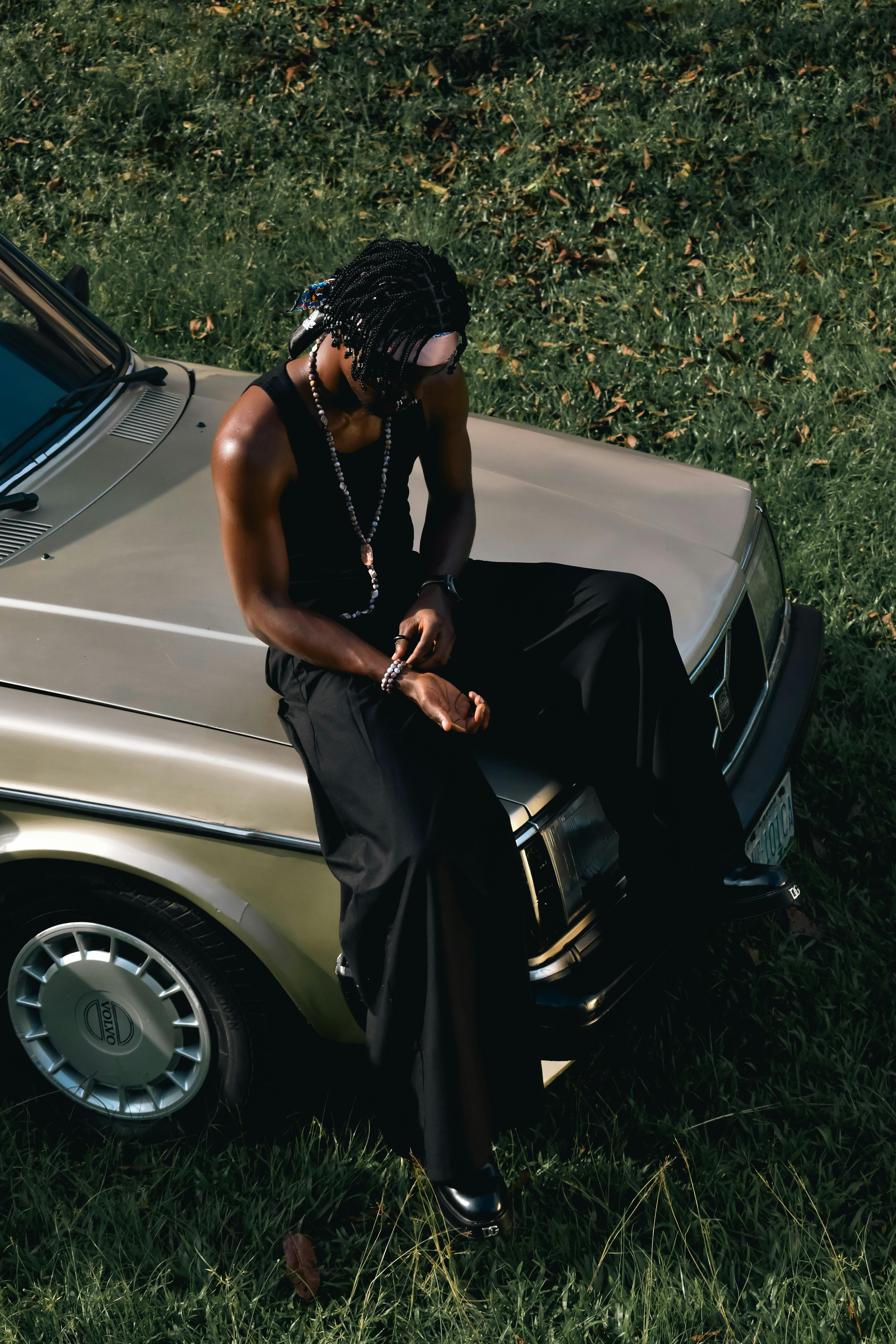 Fashionable person leaning on a vintage car outdoors in natural light.