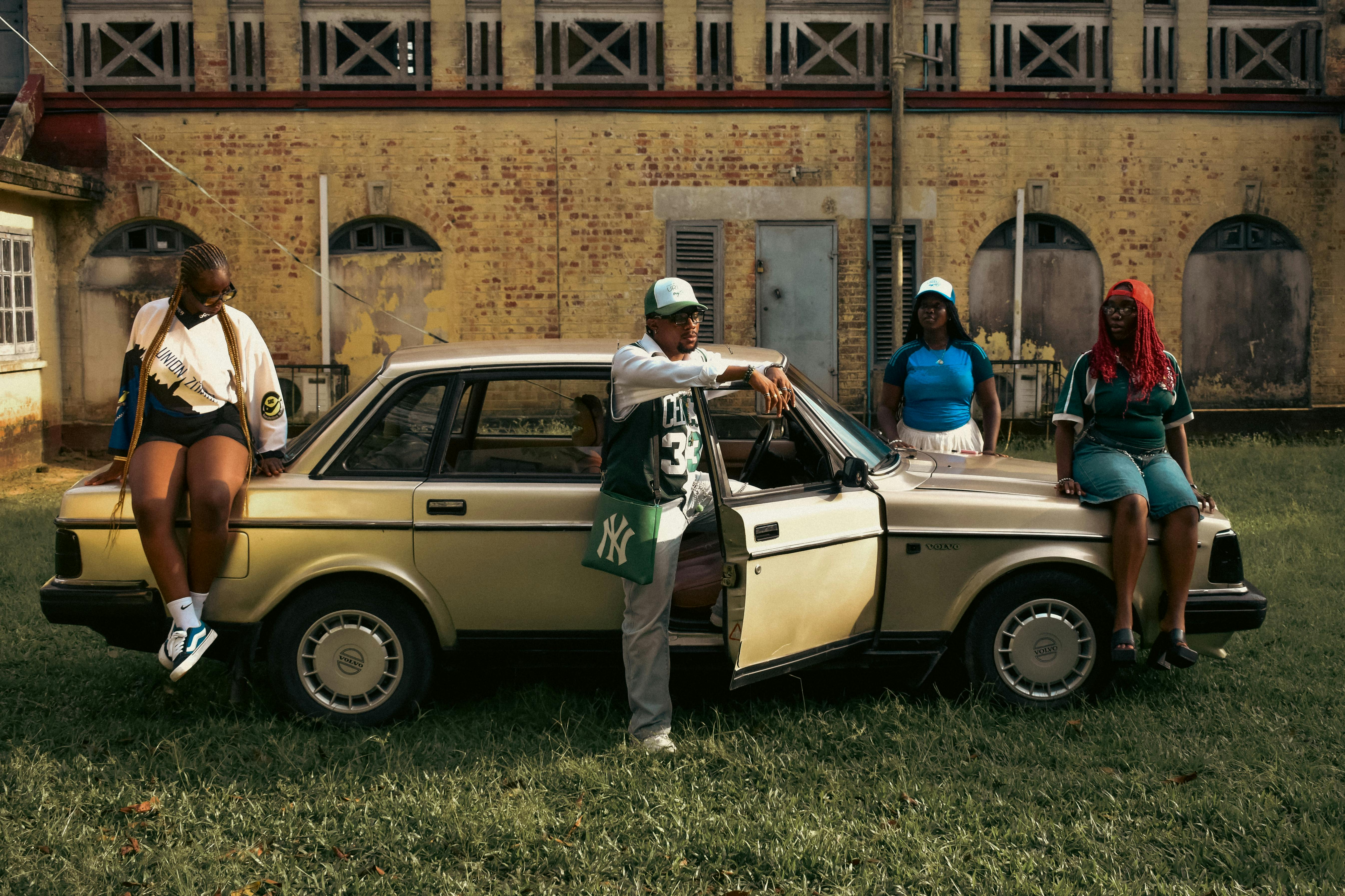 Group of friends posing with a classic vintage car in a retro urban setting, showcasing alternative culture.