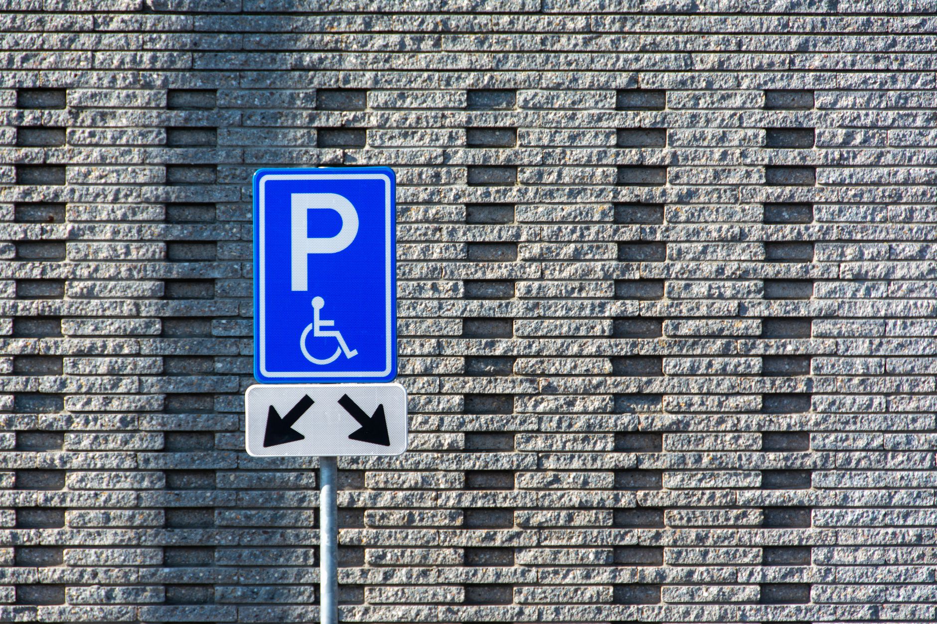 Un panneau de stationnement pour personnes handicapées se dresse contre un fond de mur en briques texturé.