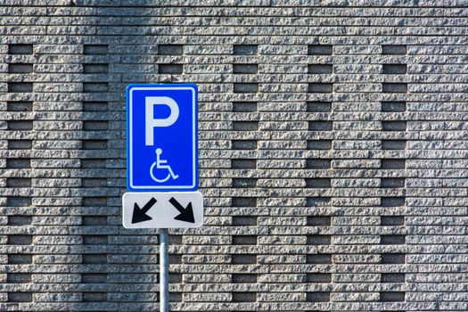 A disability parking sign stands against a textured brick wall background.
