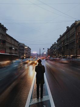 A person stands still amidst the busy traffic on a misty street in Saint Petersburg, Russia.