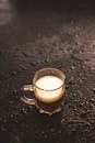 一个盛着泡沫咖啡的透明玻璃杯，放在潮湿阴暗的桌面上，营造出一种忧郁而诱人的氛围