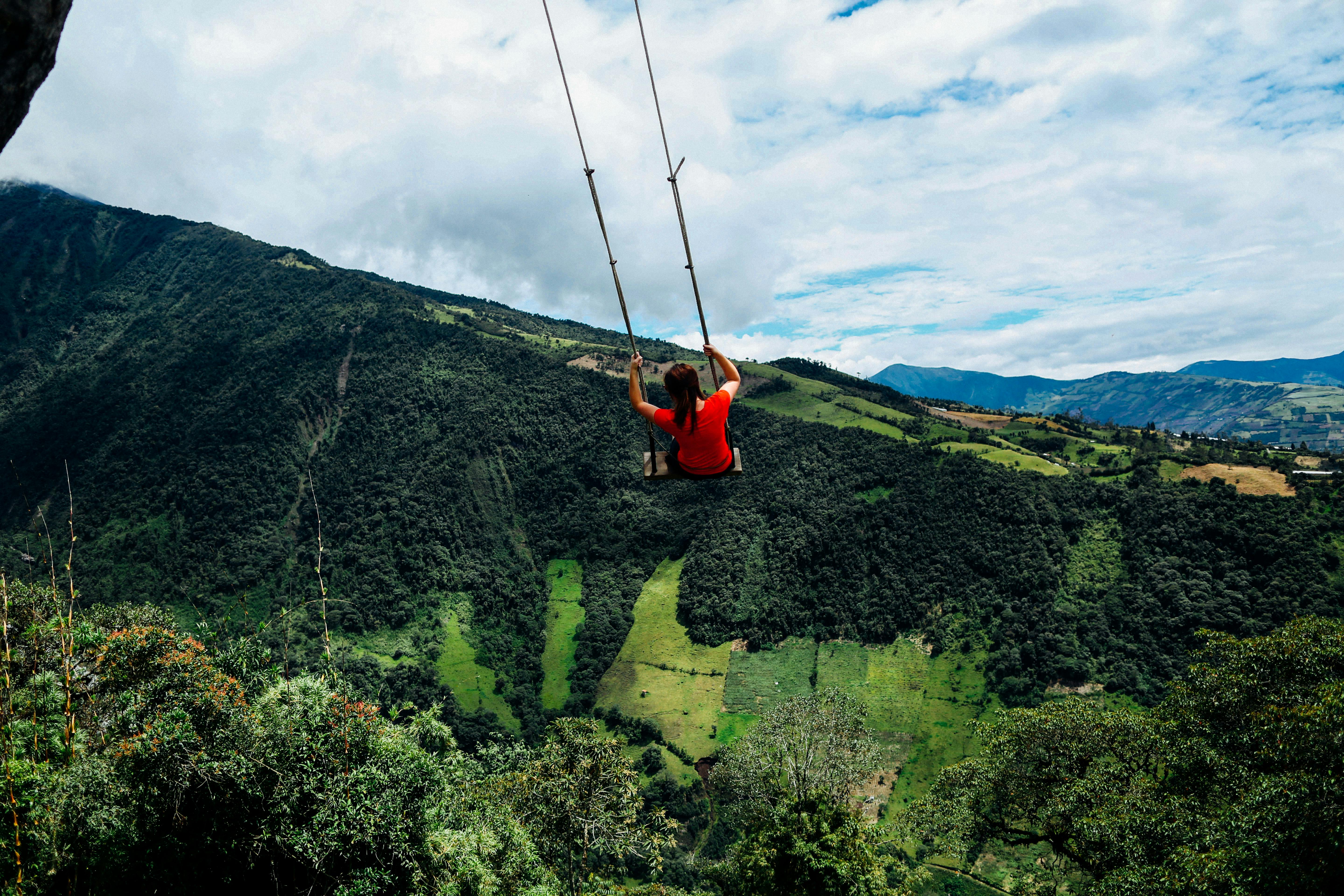 woman sitting on big outdoor swing viewing mountain under blue and white skies