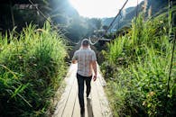 一名男子走过一座木桥，桥上阳光明媚，四周绿草如茵