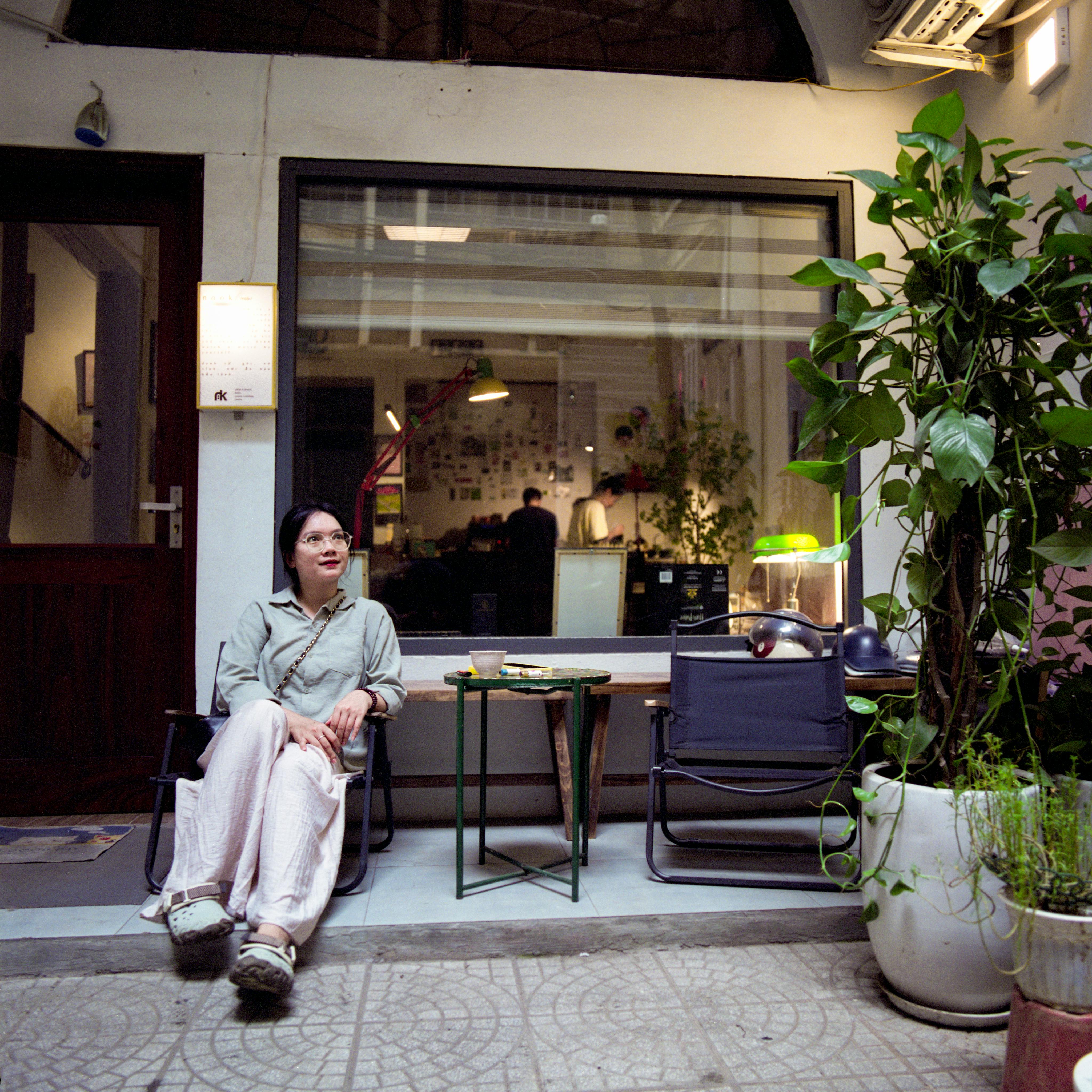 A woman casually relaxes outside a trendy cafe with indoor and outdoor elements.