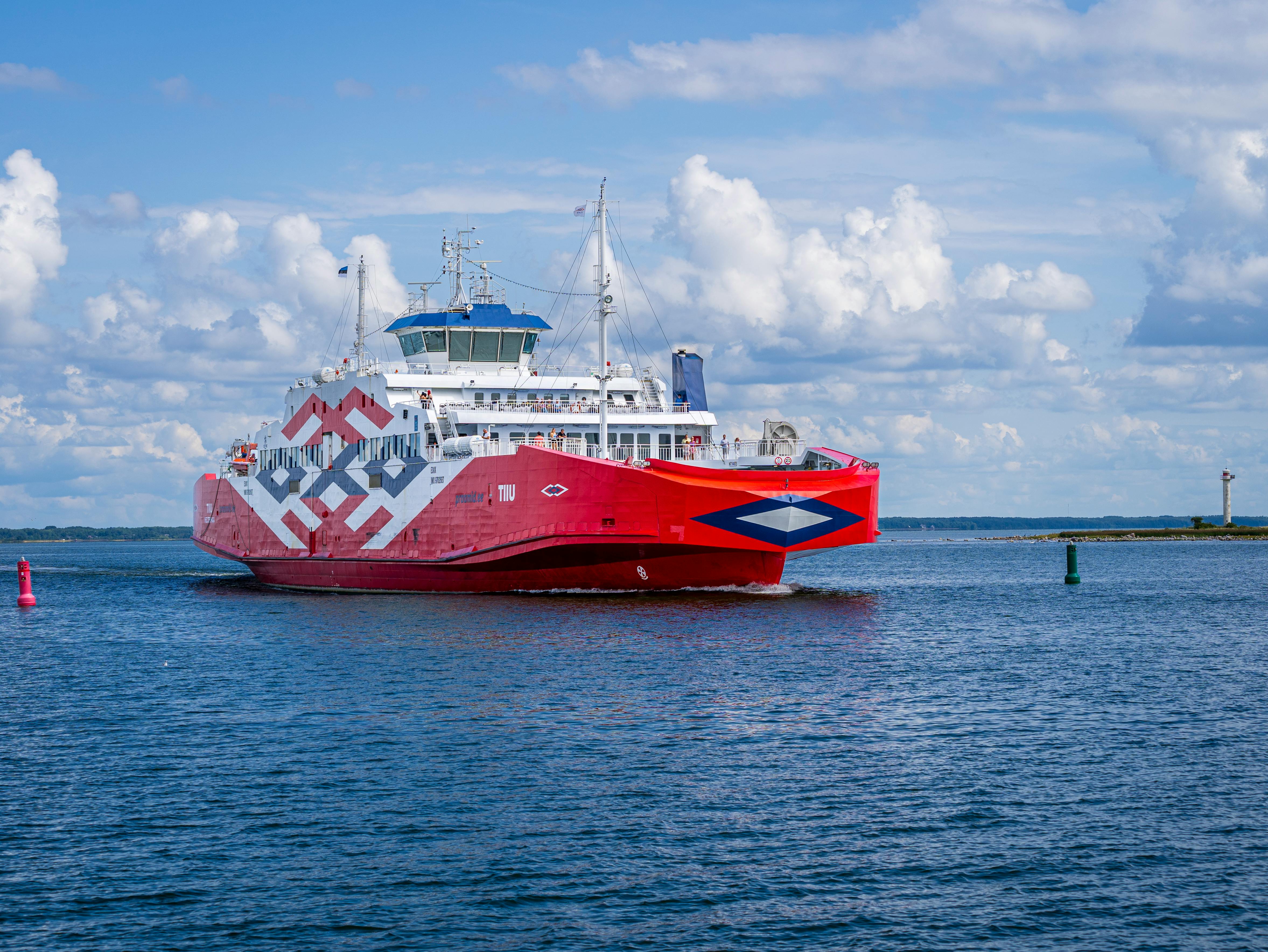 A striking red ferry sails through serene waters in Hiidenmaa, Finland, under a clear blue sky.