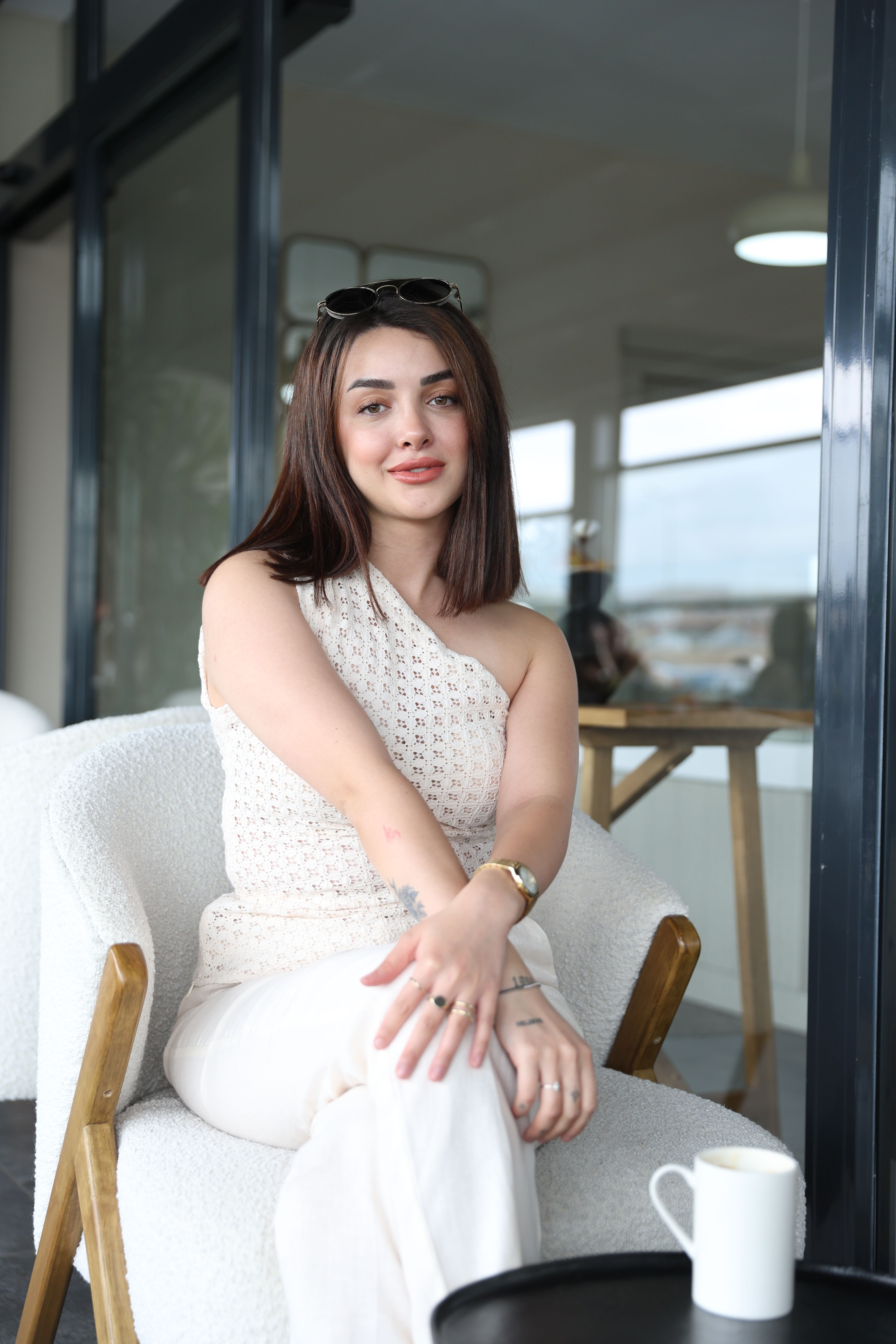 Elegant woman in white seated indoors, exuding confidence and style.