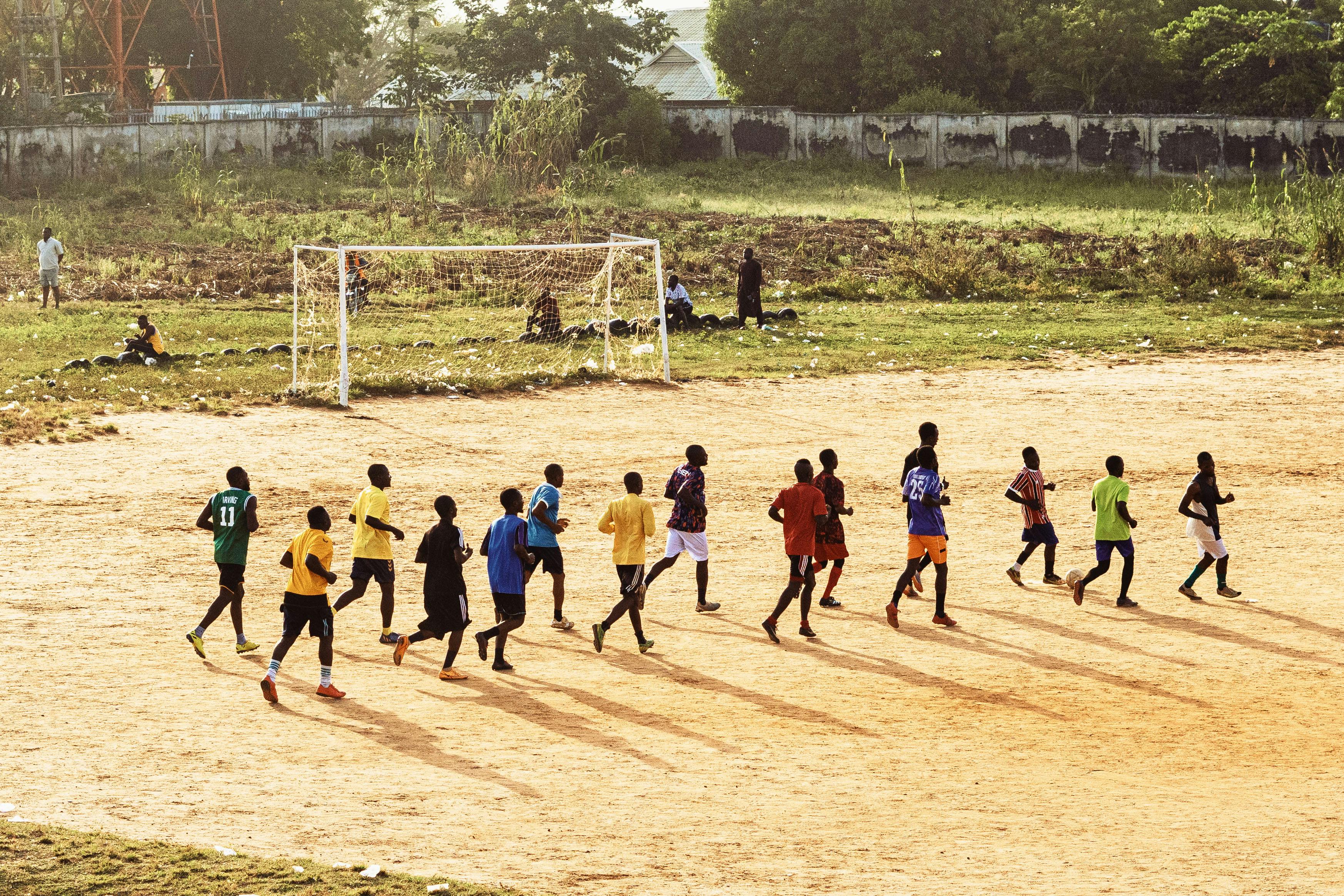 A group of young men practicing soccer on a dirt field under the sun.