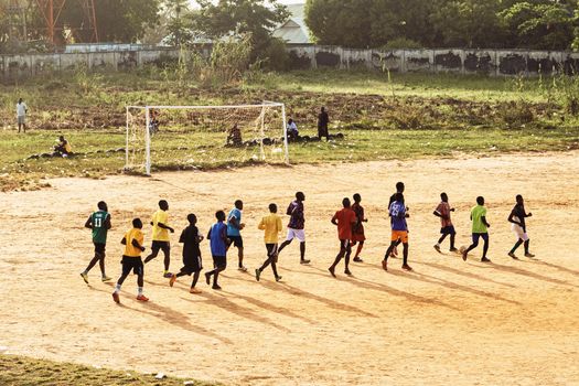 A group of young men practicing soccer on a dirt field under the sun.