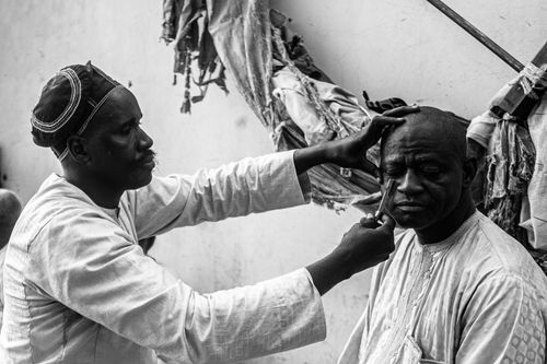 Free A barber skillfully shaves a man's head in a traditional setting, captured in black and white. Stock Photo