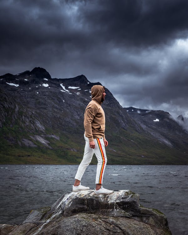 Kostenlos Person, Die Weiße Und Orangefarbene Jogginghose Und Braunes Sweatshirt Trägt, Die Auf Felsen Nahe Dem Gewässer Stehen Stock-Foto