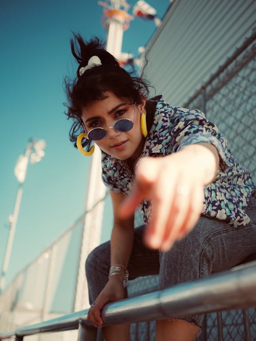 Selective Focus Photo of Woman in Floral Shirt, Grey Jeans, and Sunglasses Pointing Finger