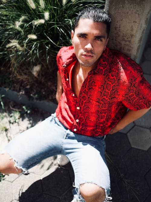 Photo of Man in Red Shirt Leaning on Stone Pillar While Squat Posing