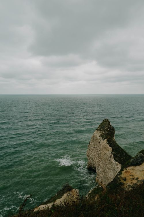 Free A captivating view of a dramatic cliff against a moody ocean under cloudy skies. Stock Photo