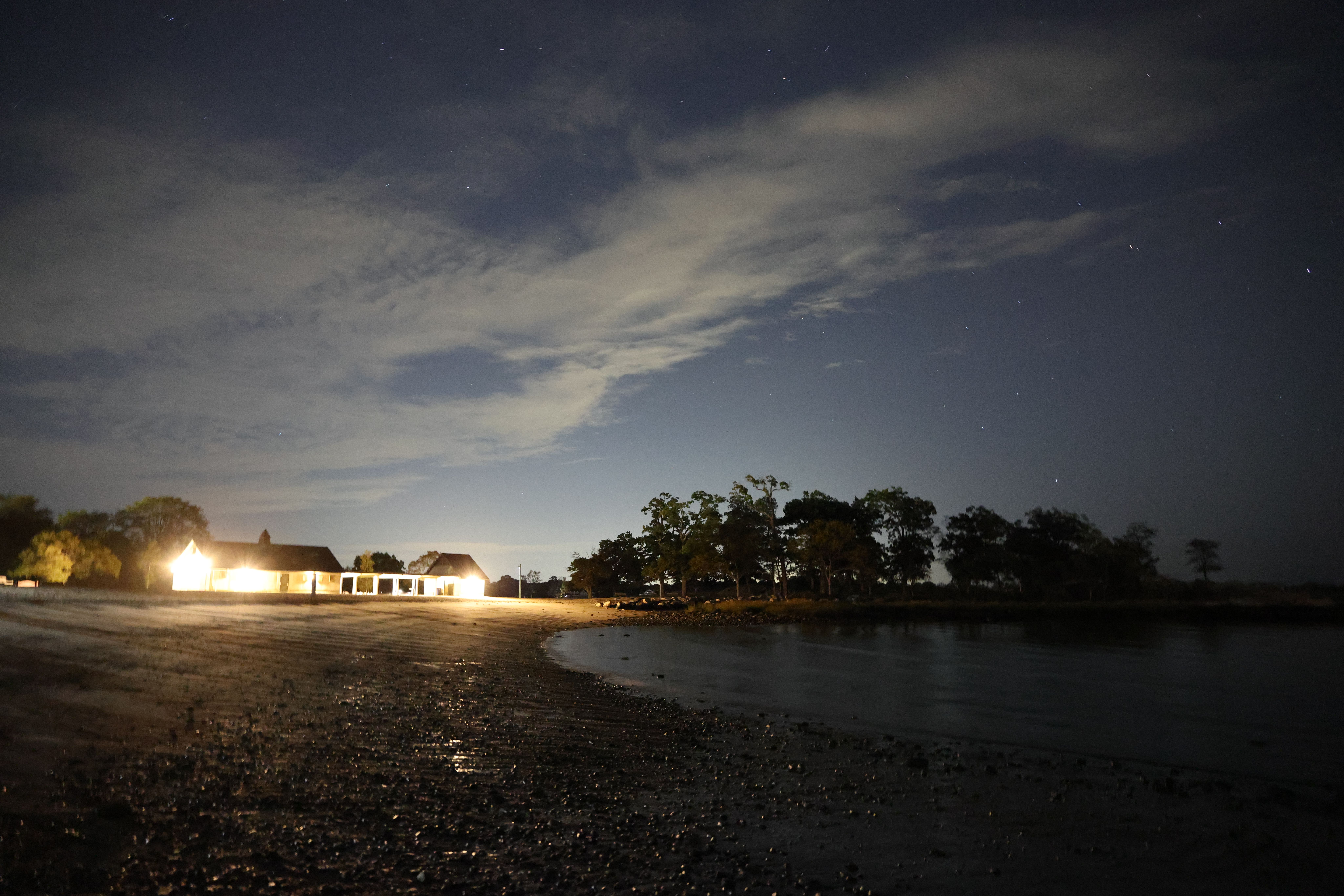 Scenic view of a coastal area at dusk in Stamford, CT, featuring an illuminated house and a calm shoreline.