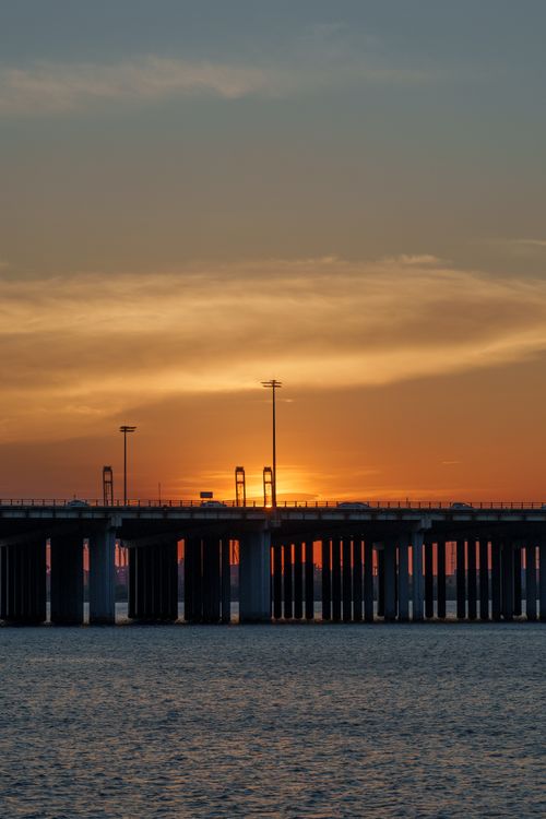 Free A stunning sunset with vivid colors behind a silhouette of a city bridge over water. Stock Photo