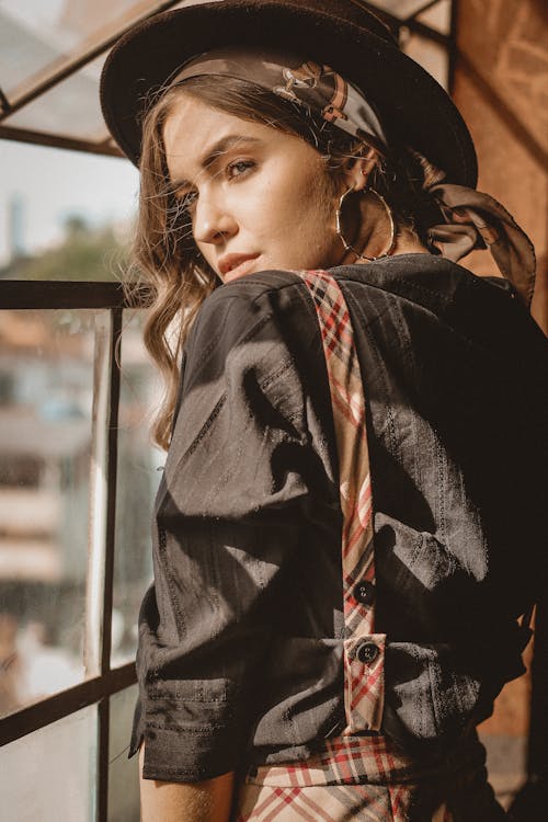 Photo of Woman in Black Top and Hat Posing by Window