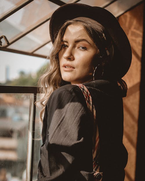 Photo of Woman in Black Top and Hat Posing by Window